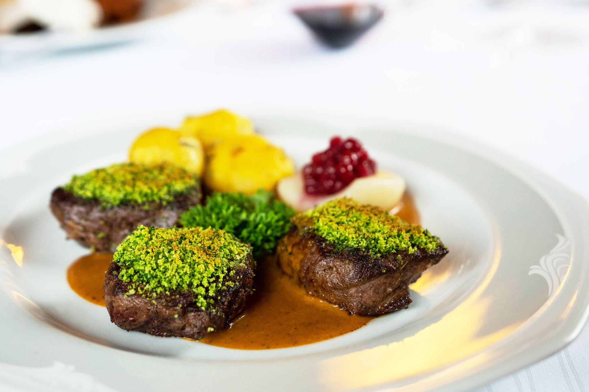 Medaillons mit Kräuterkruste, Kartoffeln und Preiselbeer-Birne auf dem Teller
